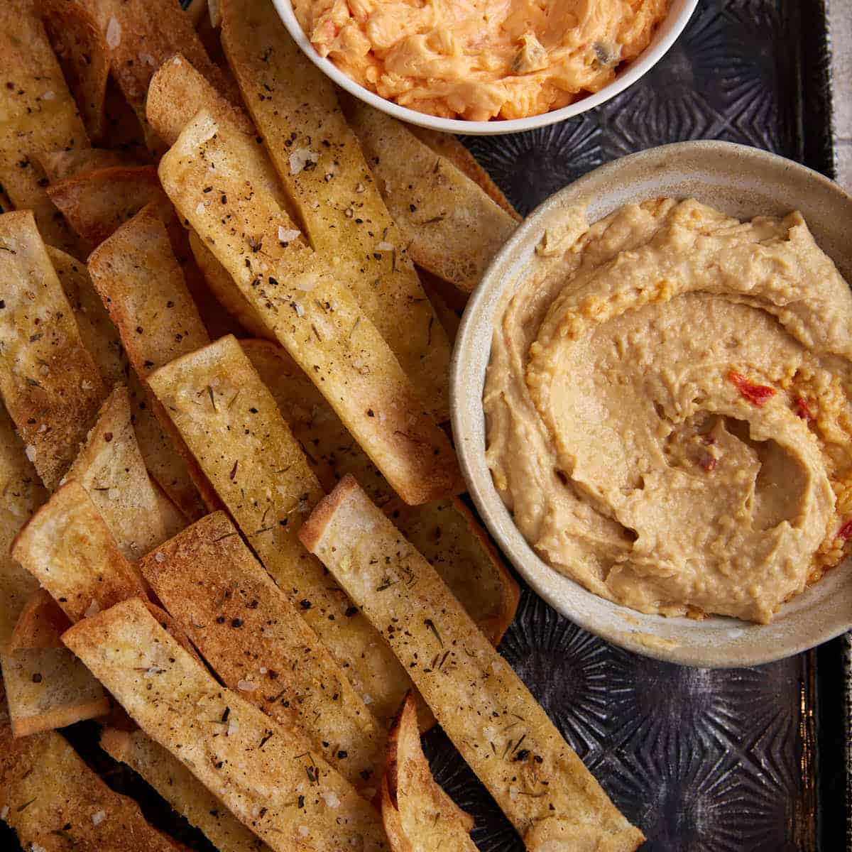 Seasoned pita chips next to a bowl of hummus and pimento cheese.