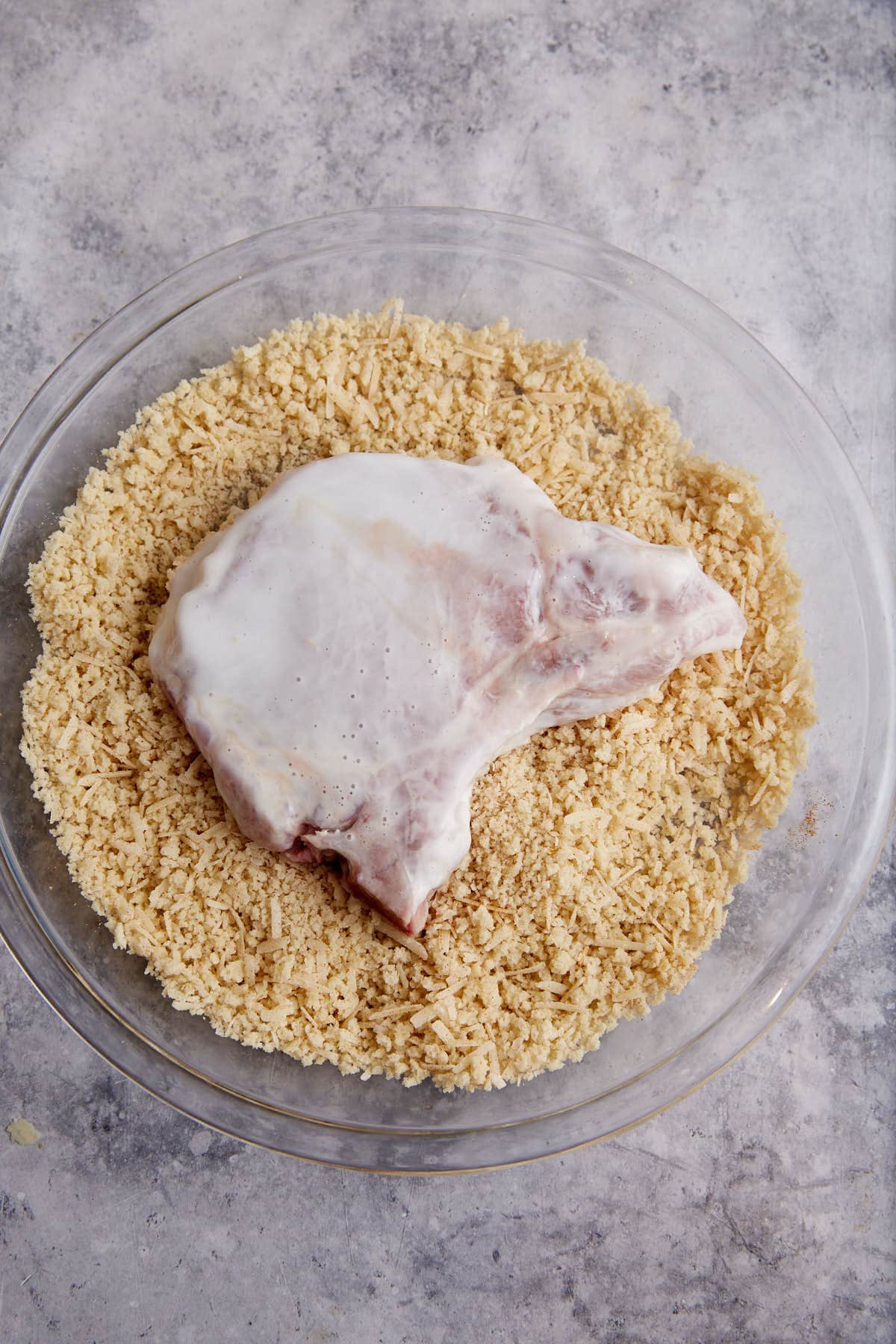 A buttermilk soaked pork chop on top of a panko mixture.
