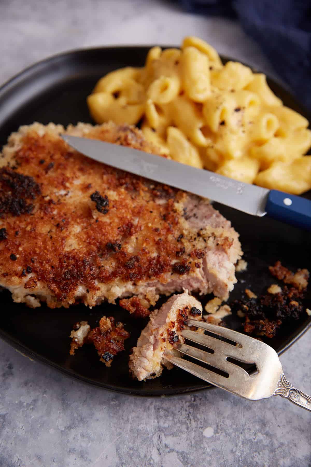 A fork in a bite of a fried pork chop.