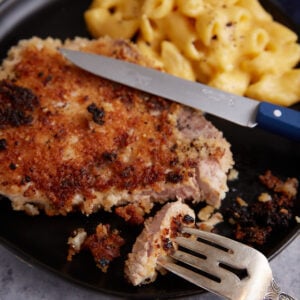 A fork in a bite of a fried pork chop.