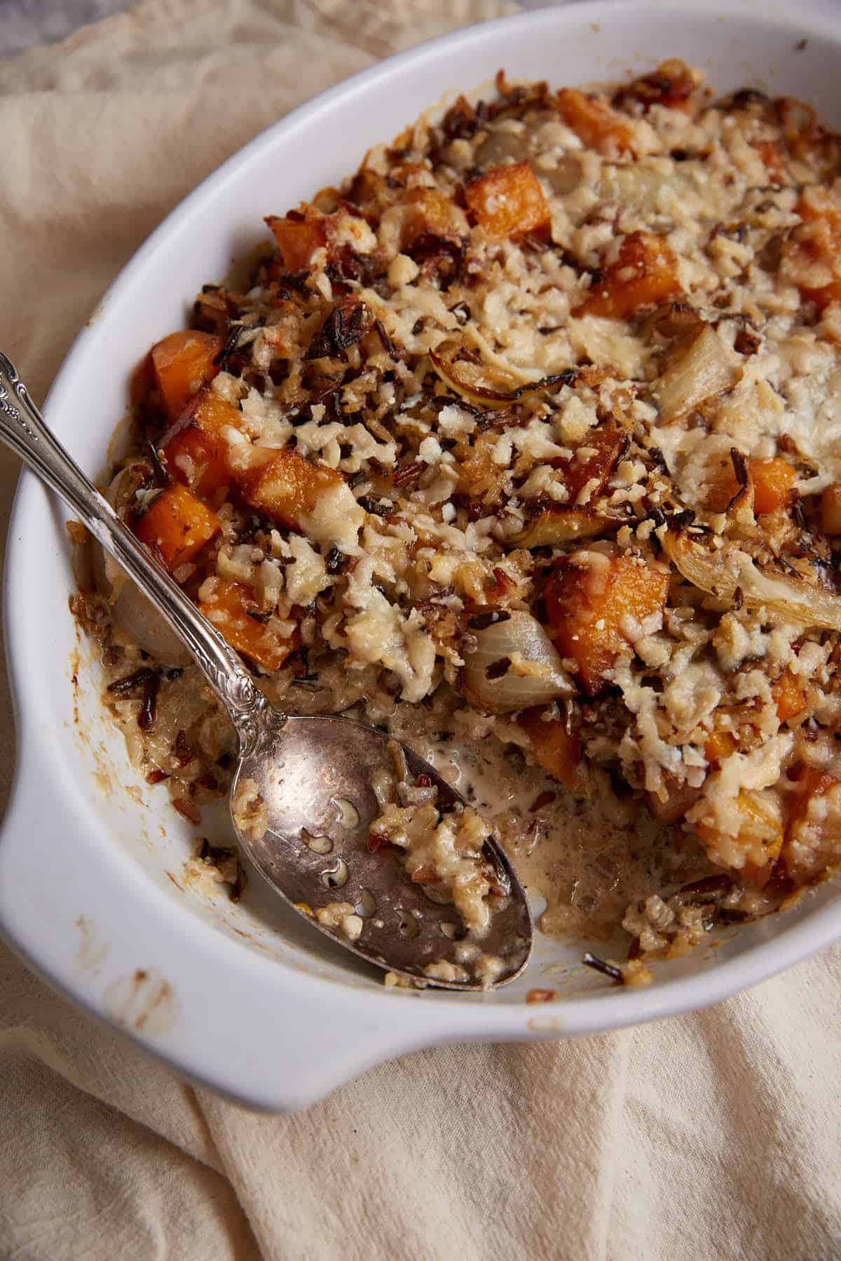 A serving spoon in a baking dish of butternut squash casserole.