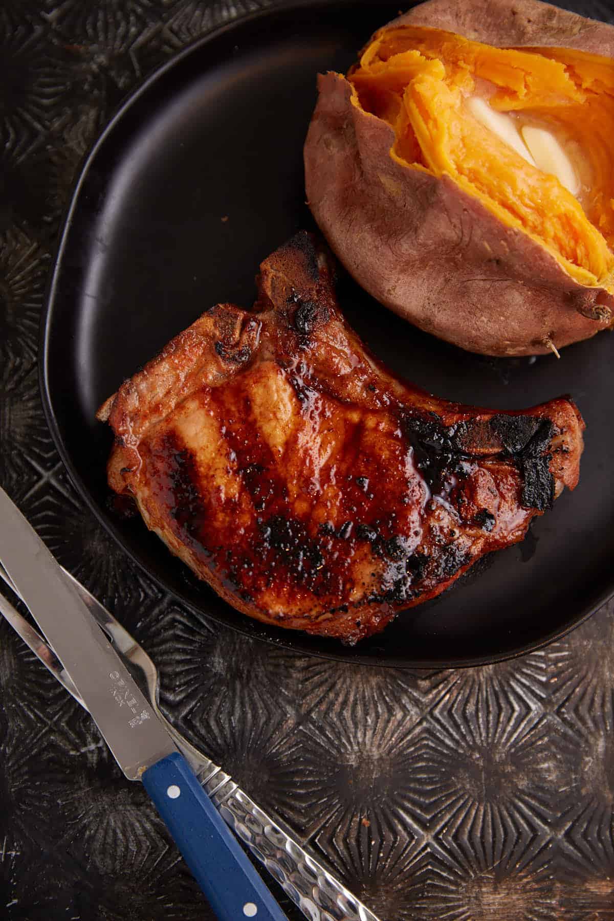 A grilled pork chop next to a sweet potato on a plate.