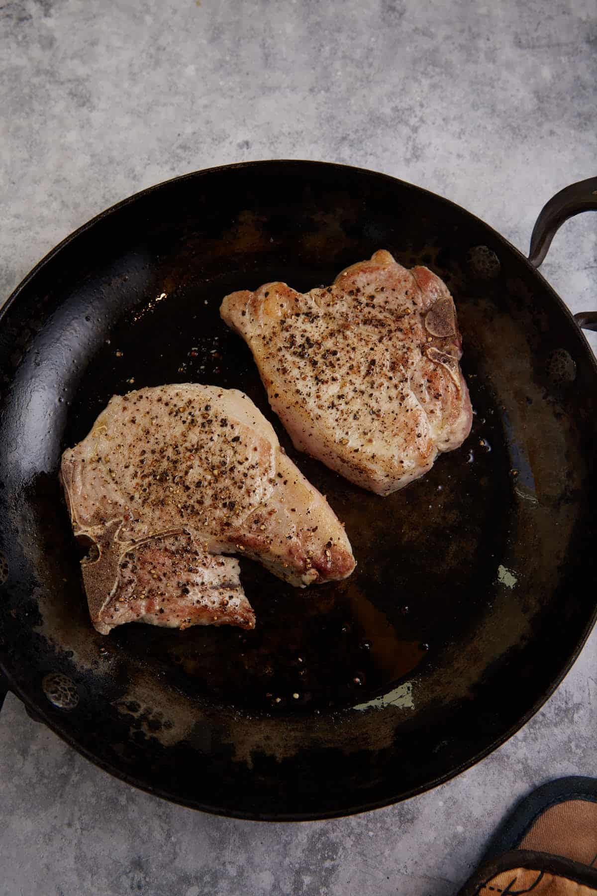 Two pork chops seared in a skillet.