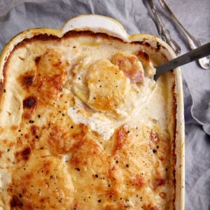 A serving spoon in a casserole dish of scalloped potatoes and ham.