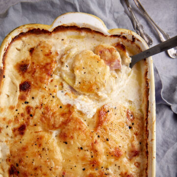 A serving spoon in a casserole dish of scalloped potatoes and ham.