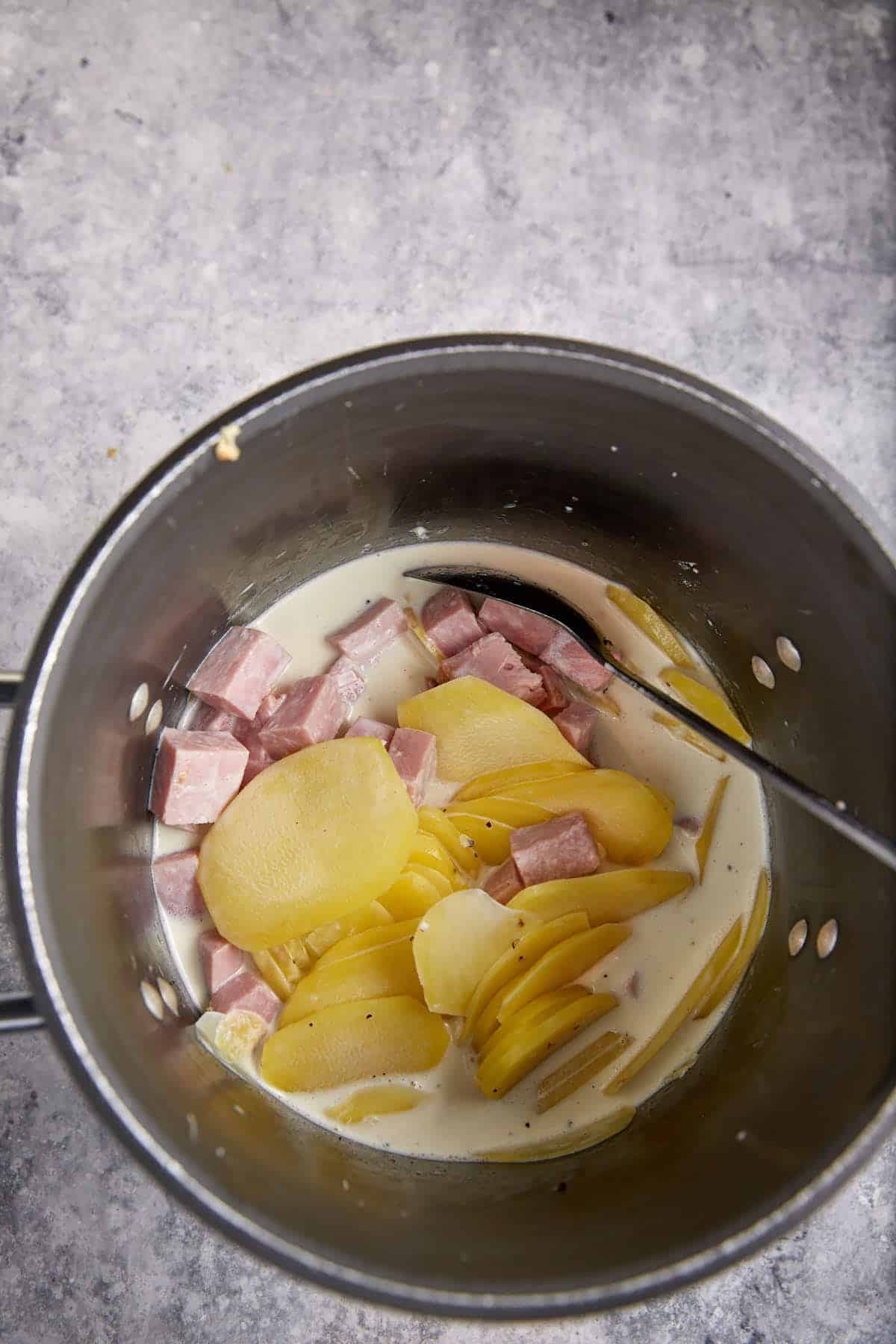 Ham added to a pot of potatoes and cream.