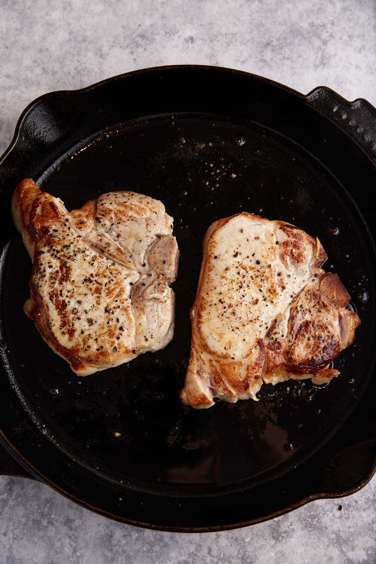 Two pork chops browned in a skillet.