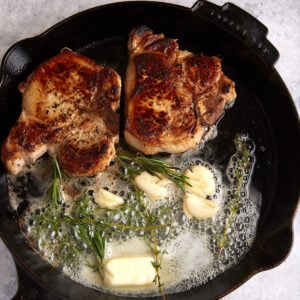A skillet of pork chops with garlic butter and herbs.