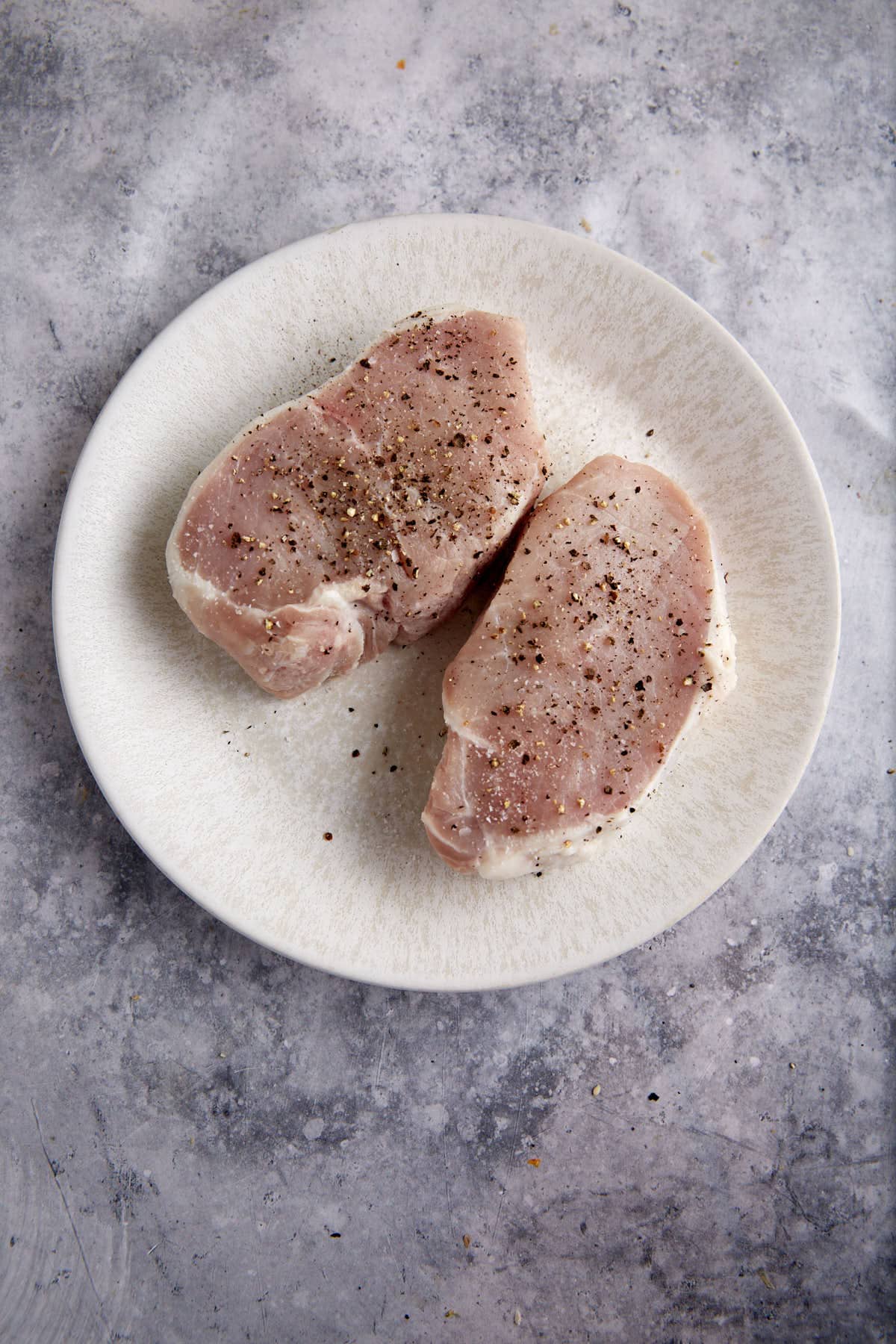 Two pork chops with salt and pepper.