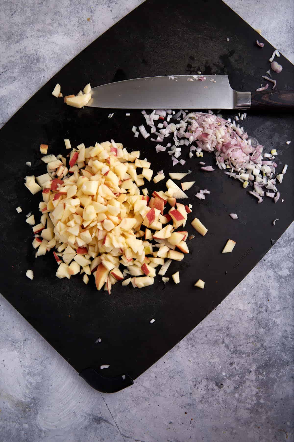Chopped apples and shallots on a cutting board.