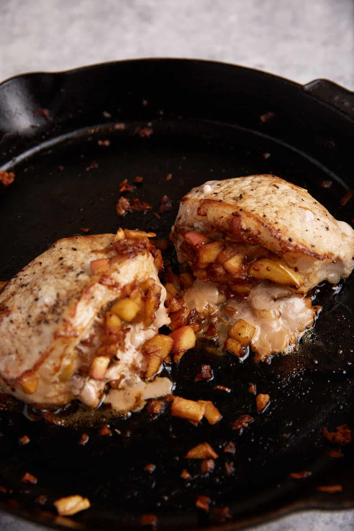 A skillet with two corn chops stuffed with apples.