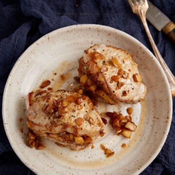 Two baked pork chops with apples on a plate.
