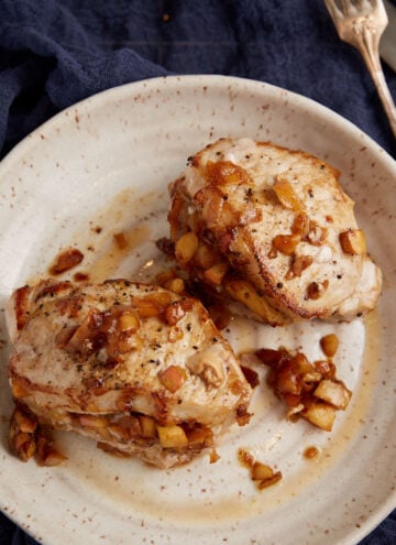 Two baked pork chops with apples on a plate.