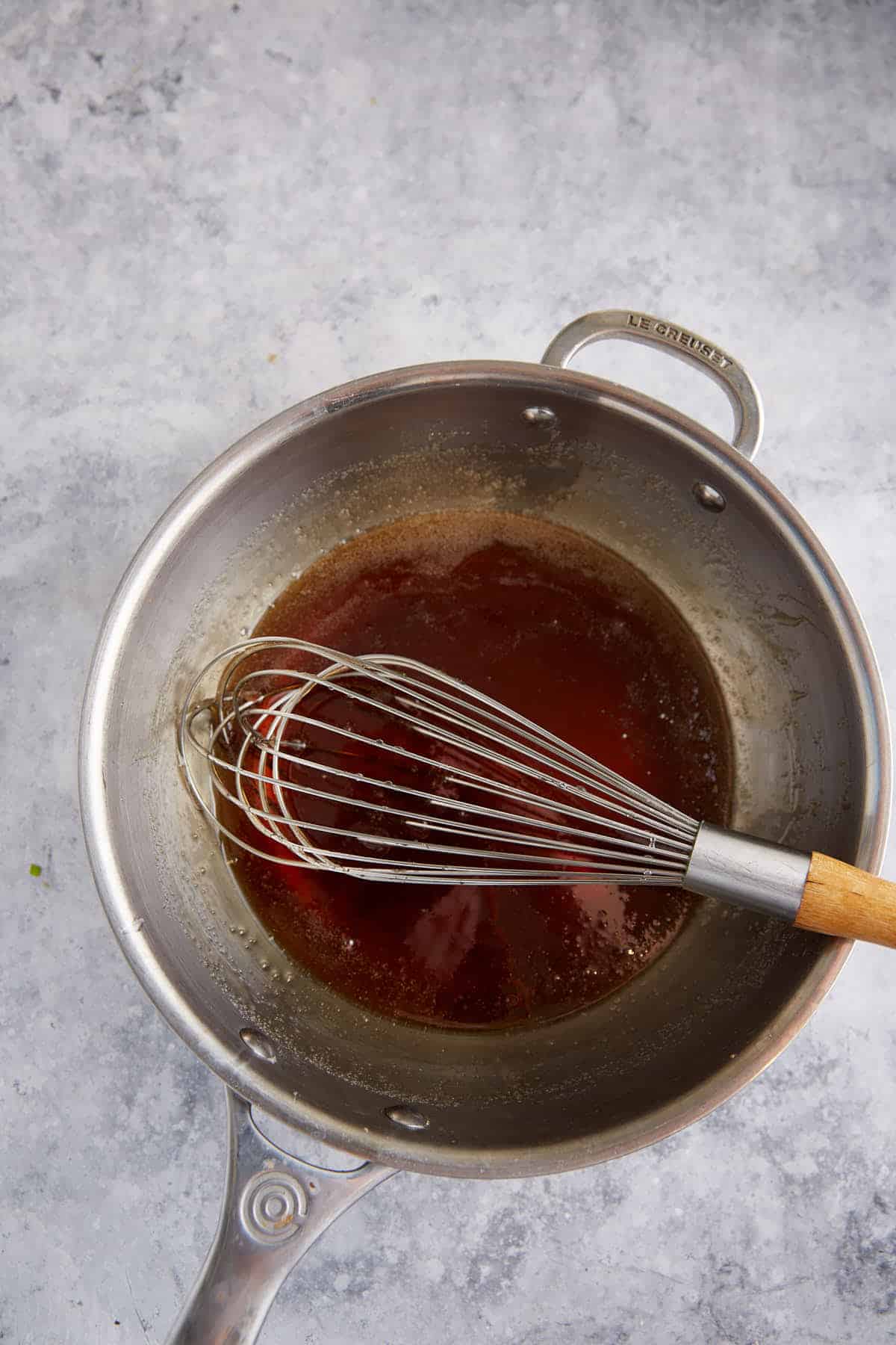 Caramel sauce in a saucepan with a whisk.