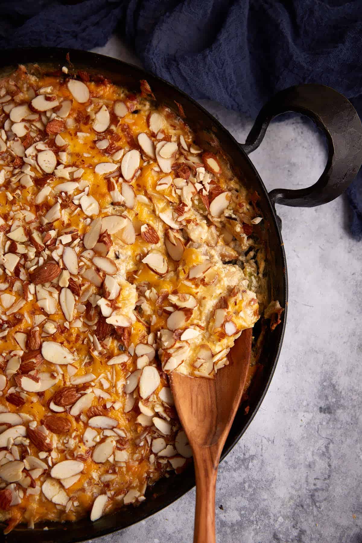 A skillet of chicken and wild rice casserole with a wooden spoon.