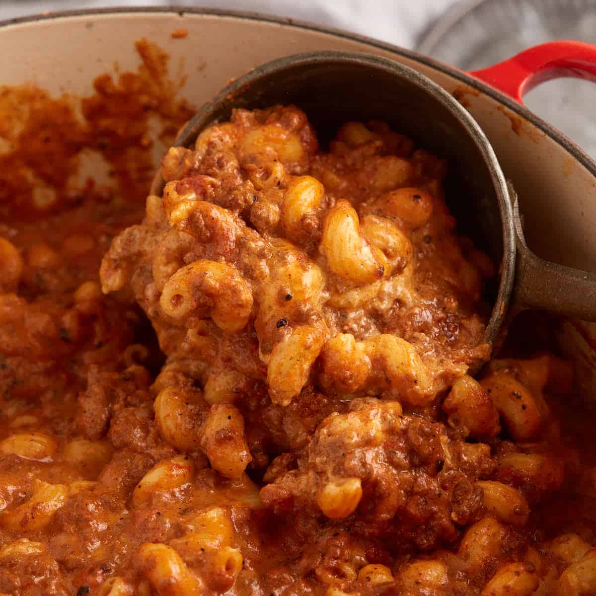 A Dutch oven with chili mac and cheese with a soup ladel.