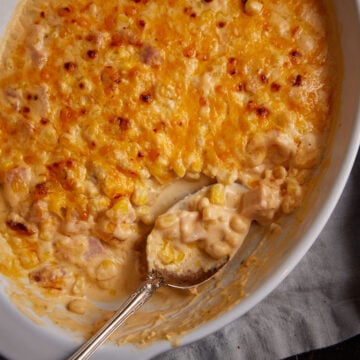 A serving spoon in a baking dish of cheese corn casserole.