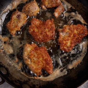 Pork cutlets cooking in oil in a skilet.