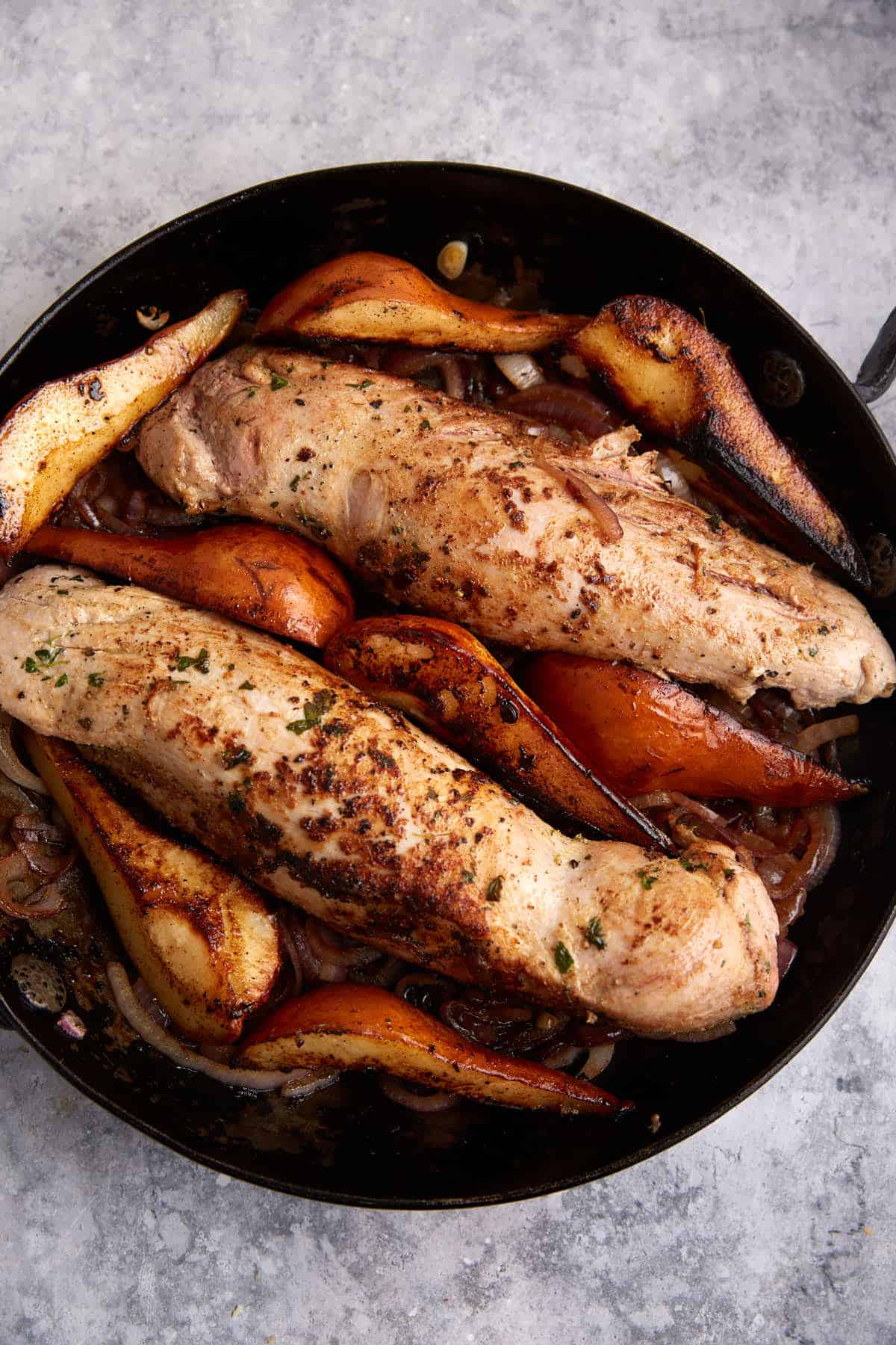 Pork added on top of onions with pears in a skillet.