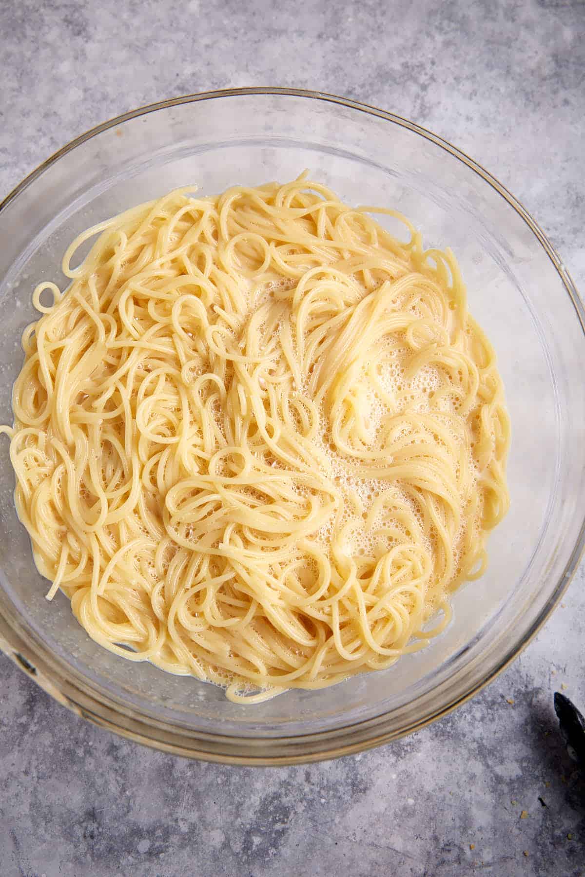 Pasta mixed with eggs and milk in a mixing bowl.