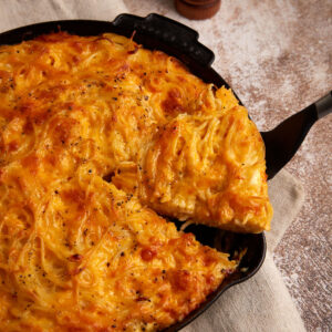 A slice of spaghetti pie casserole being removed from a skillet.