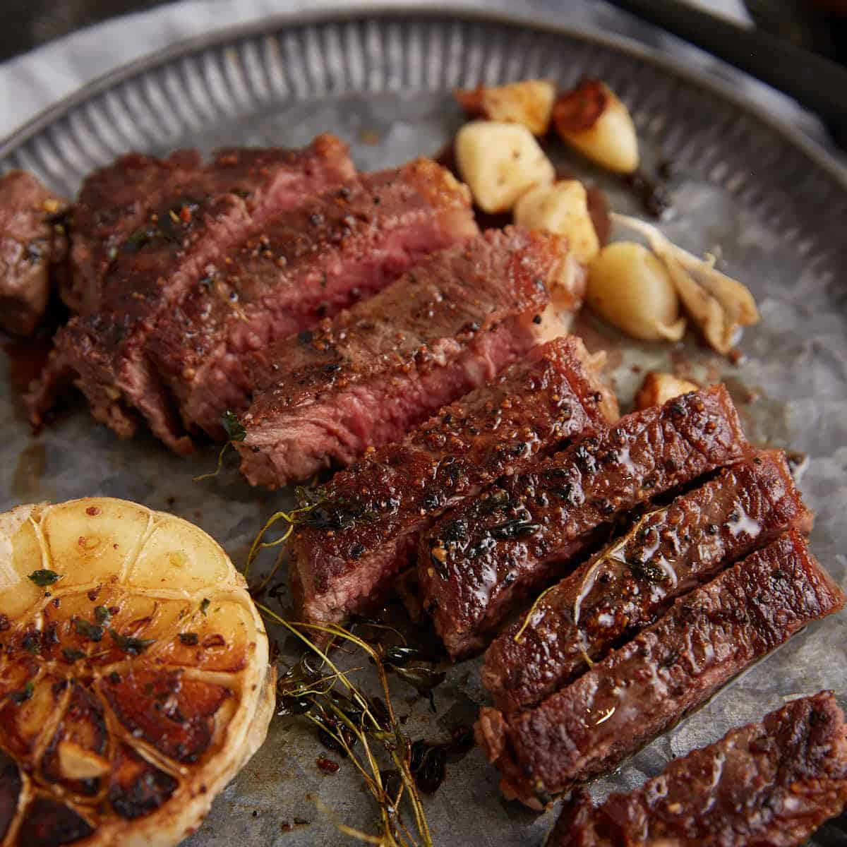 A sliced pan seared steak next to garlic on a platter.