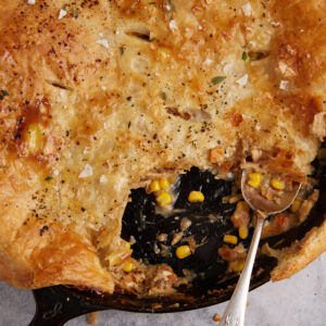A skillet of chicken pot pie with puff pastry with a serving spoon.