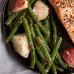 A plate of green bean salad with potatoes next to salmon.