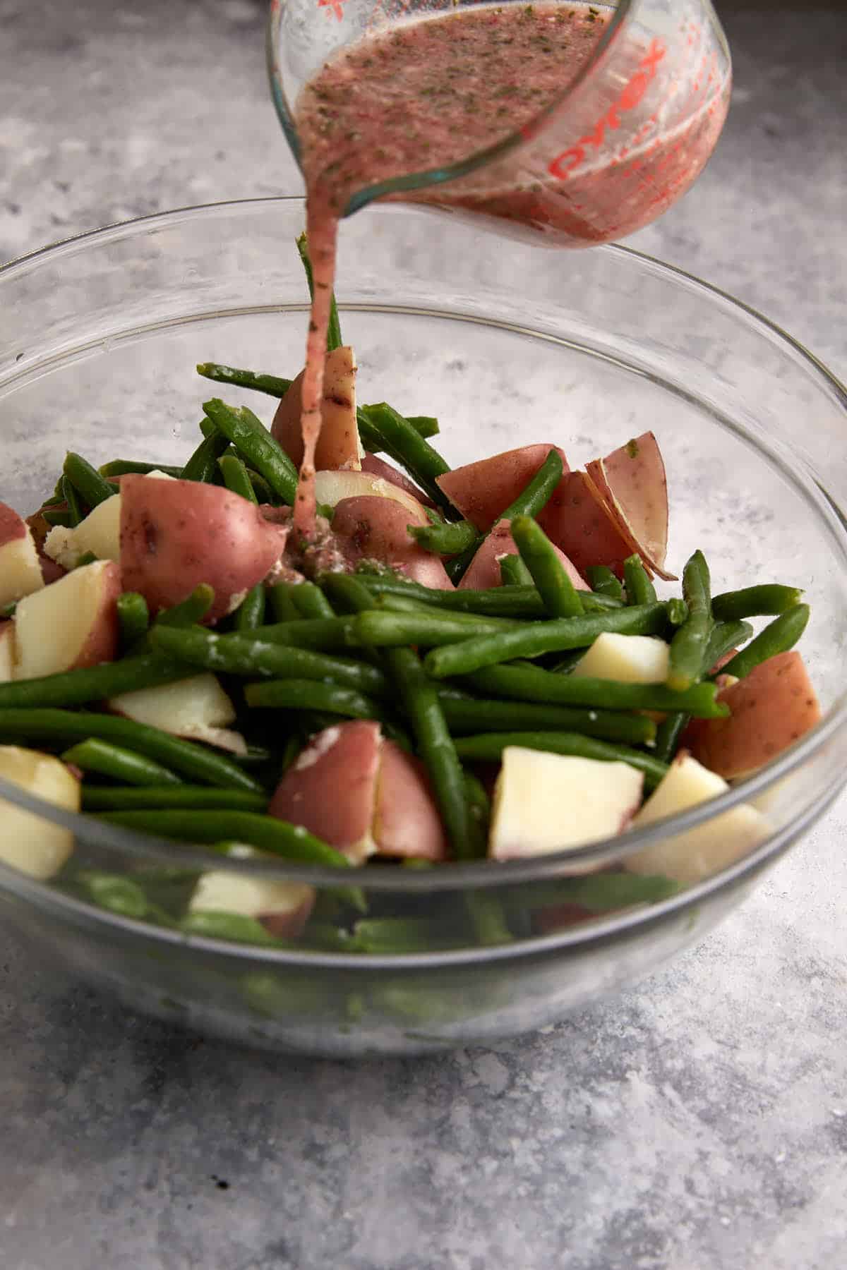Salad dressing being poured over green bean salad.