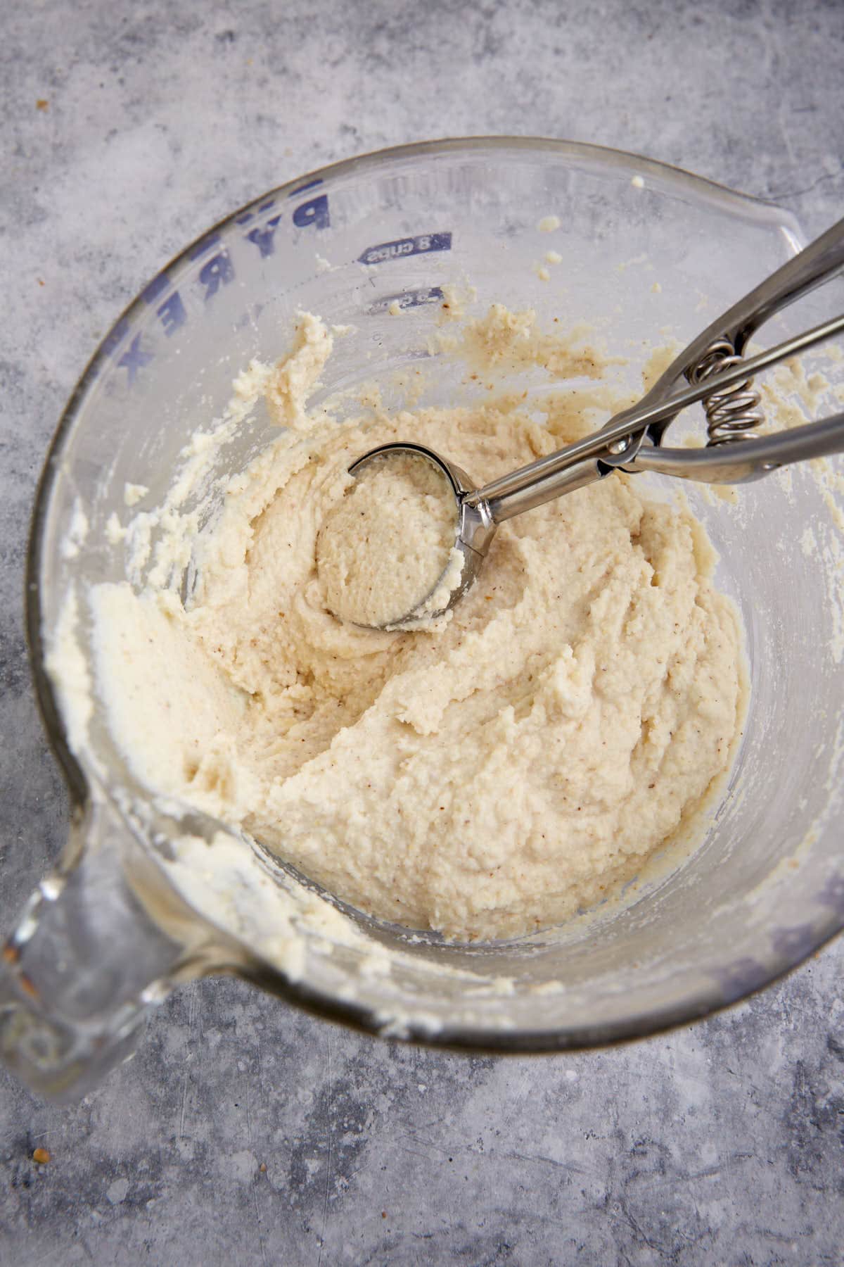 An ice cream scoop in a bowl of cornbread batter.