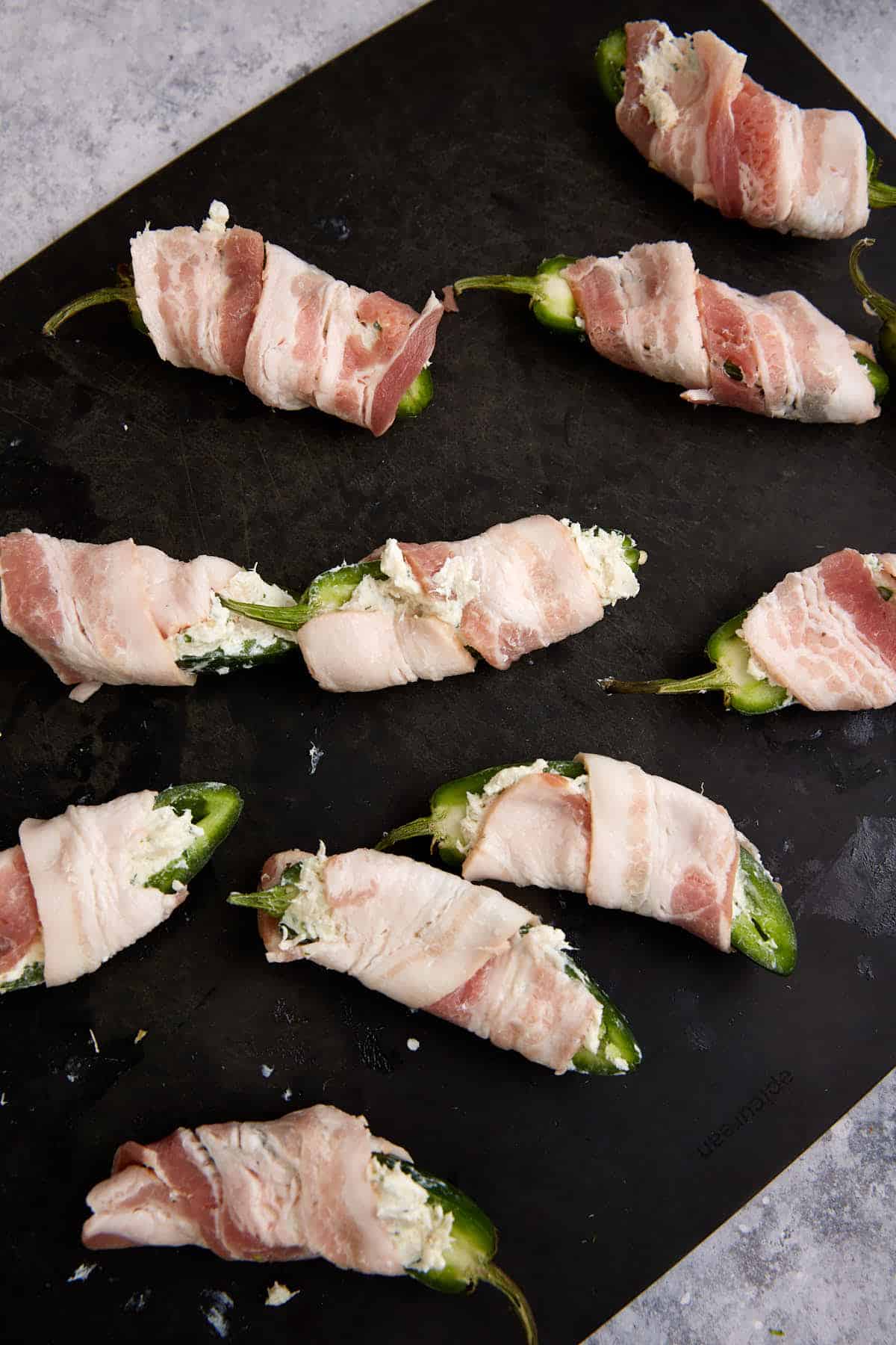 Stuffed peppers wrapped in bacon on a cutting board.