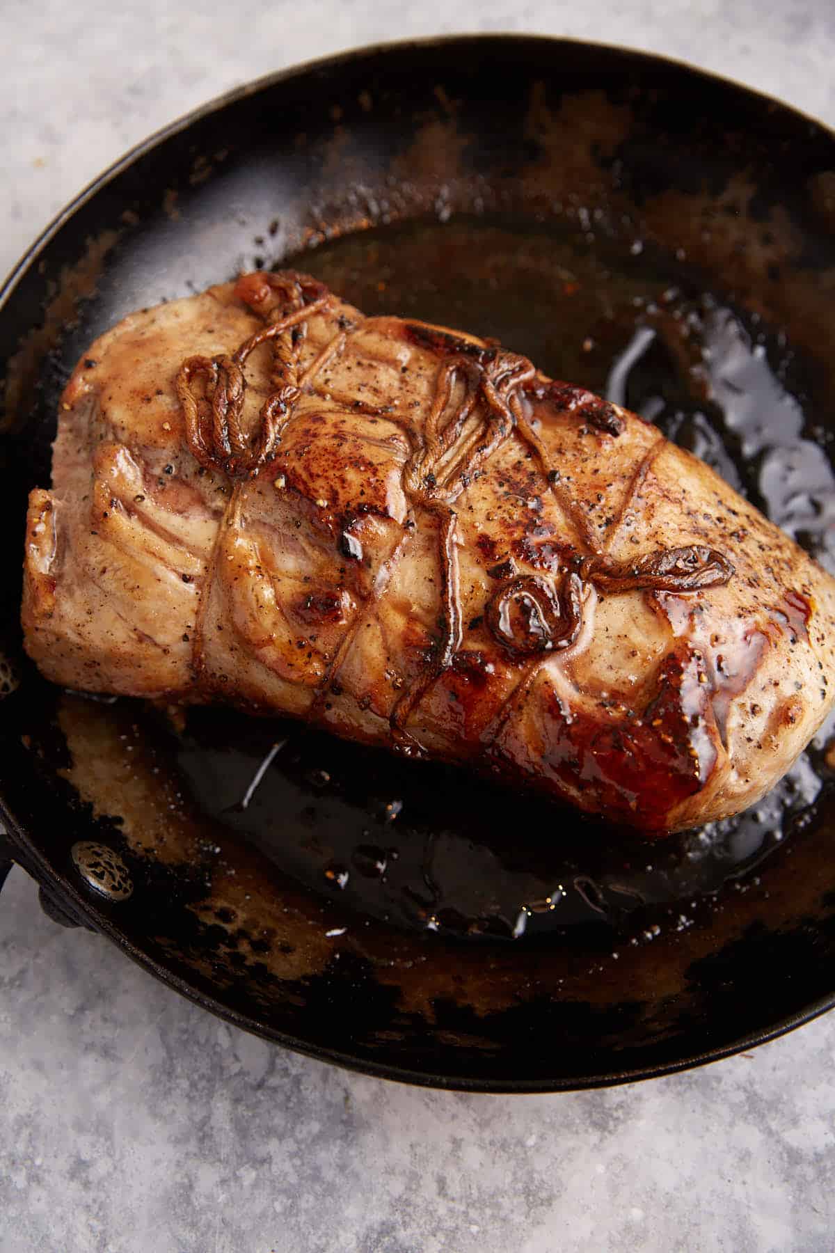 A pork roast coated in a maple glaze in a skillet.