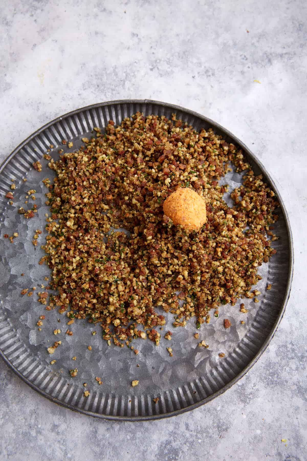 A cheese ball being rolled in bacon and pecans.