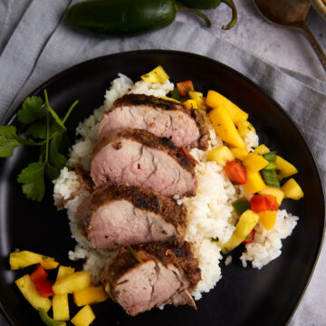A plate of sliced pork tenderloin on rice with pineapple salsa.