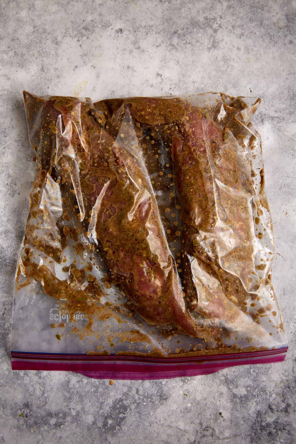 Two pork tenderloins in a bag with marinade.