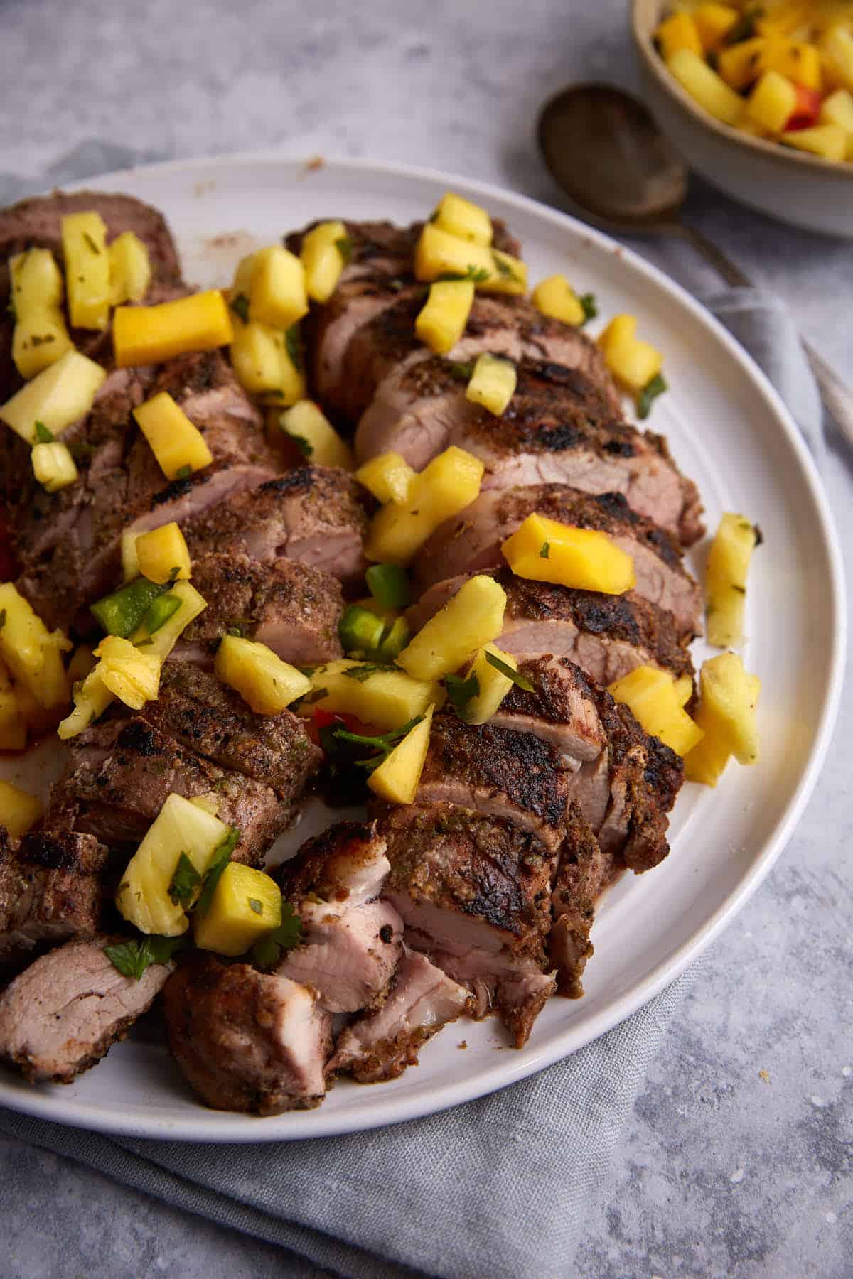 A serving platter of grilled pork tenderloin with salsa.