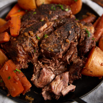 A tender pot roast on a serving platter with carrots and potatoes.