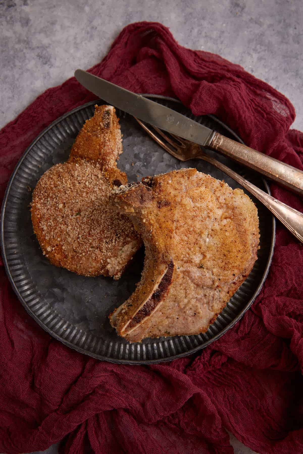 Two pork chops on a plate with a knife and fork. 