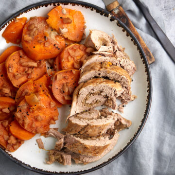 A platter of sliced stuffed pork tenderloin next to sweet potatoes.