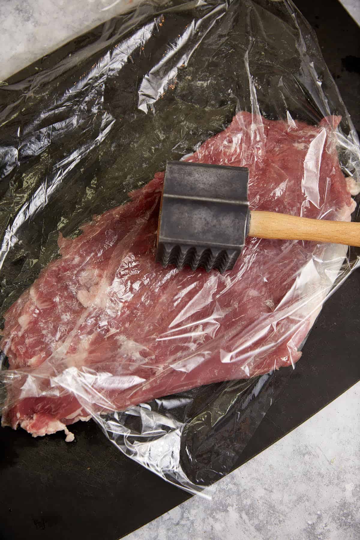 A meat tenderizer on a pounded piece of pork.