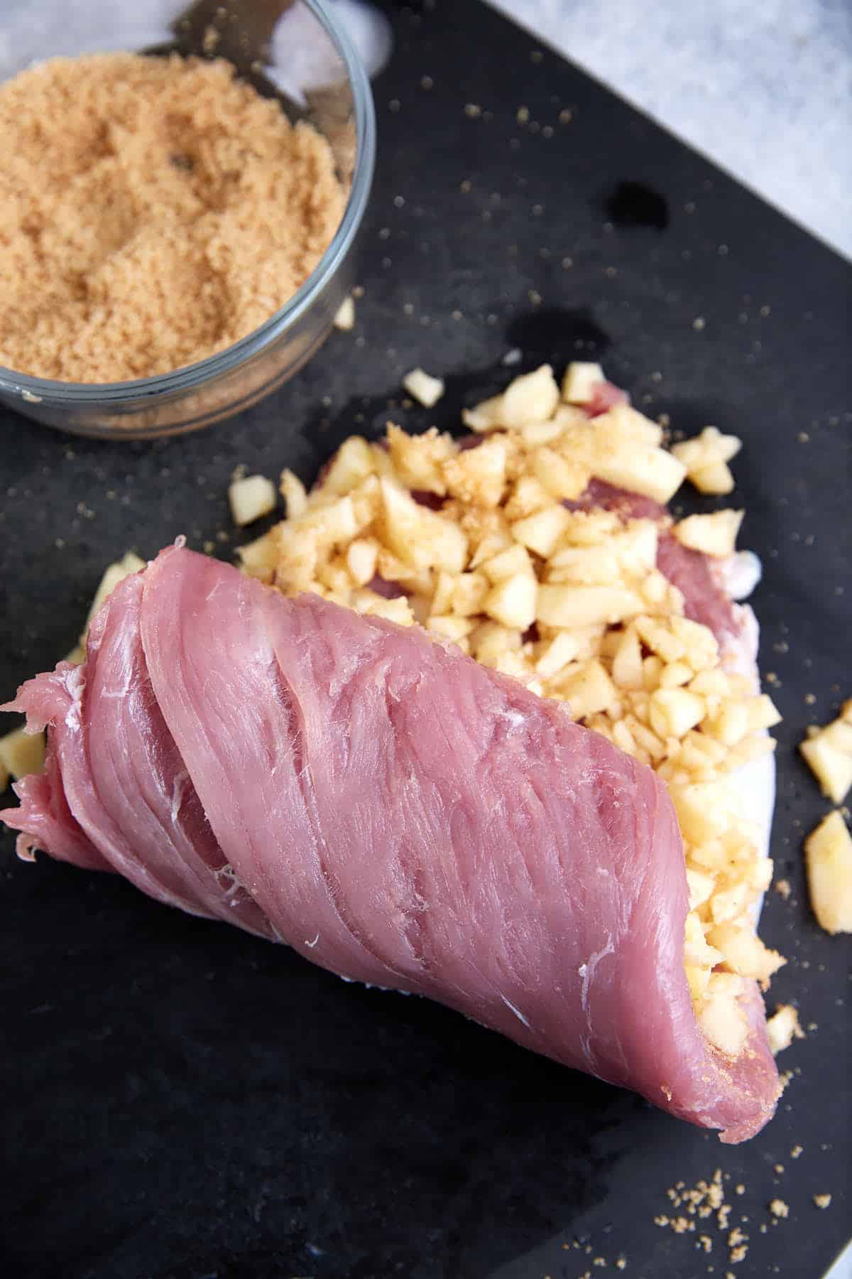 A pork tenderloin being rolled up with apples.