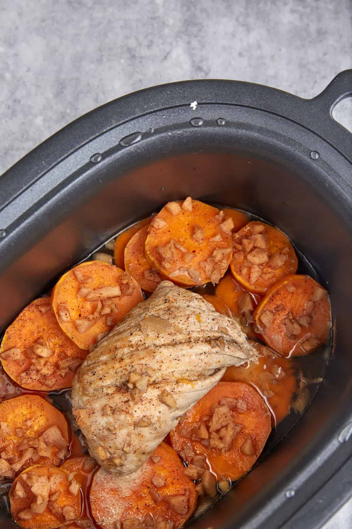 A cooked pork tenderloin on potatoes in a slow cooker.