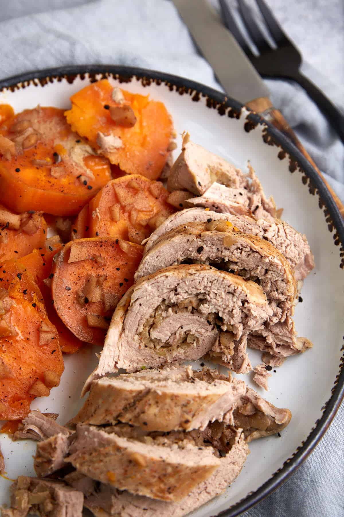 A platter of sliced pork tenderloin next to cooked sweet potatoes. 
