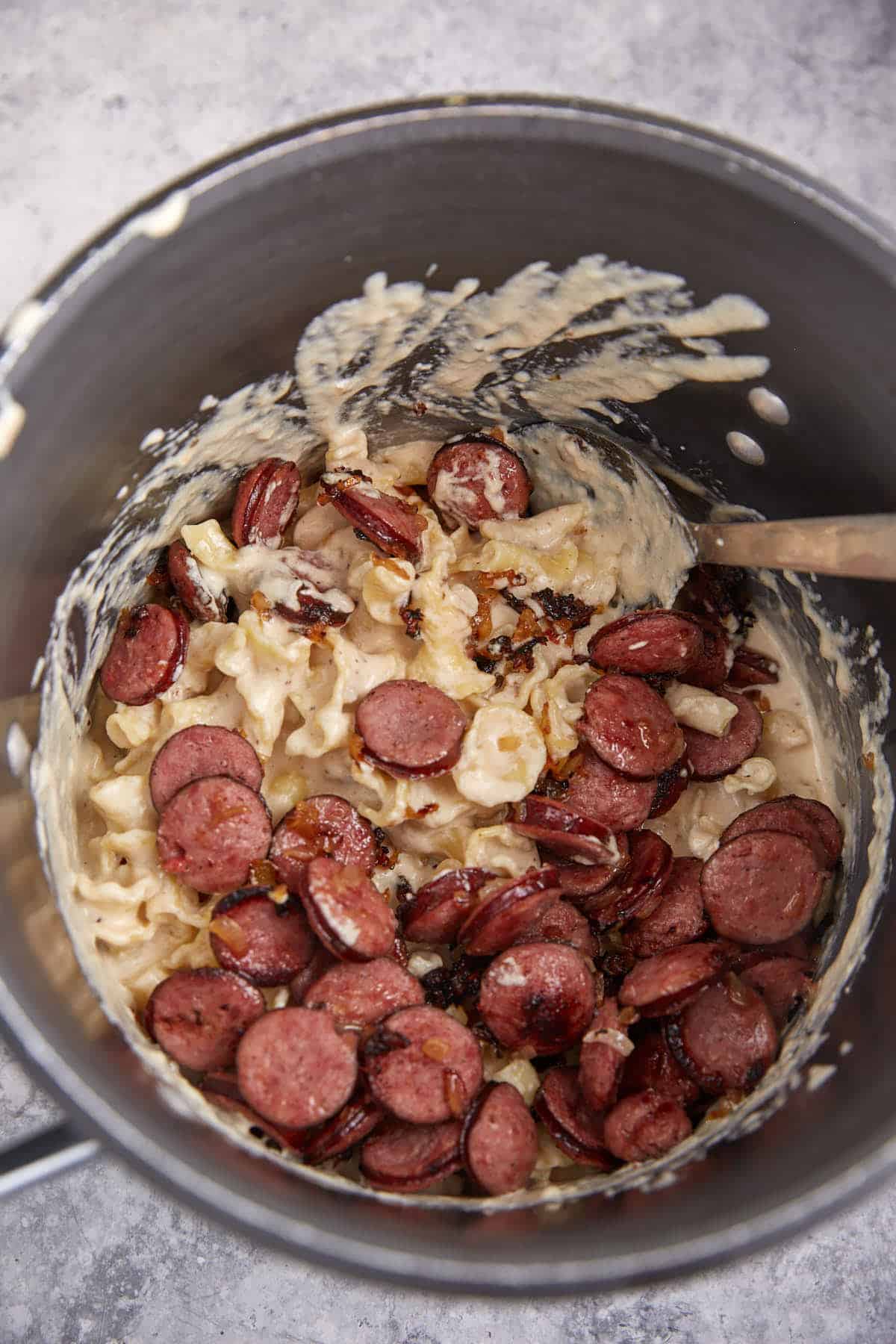 Sausage added to a pot of macaroni and cheese.