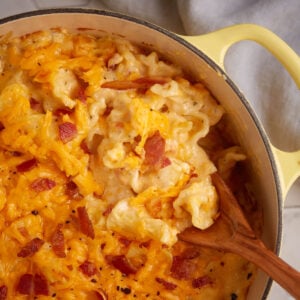 A Dutch oven of bacon mac and cheese with a wooden spoon.