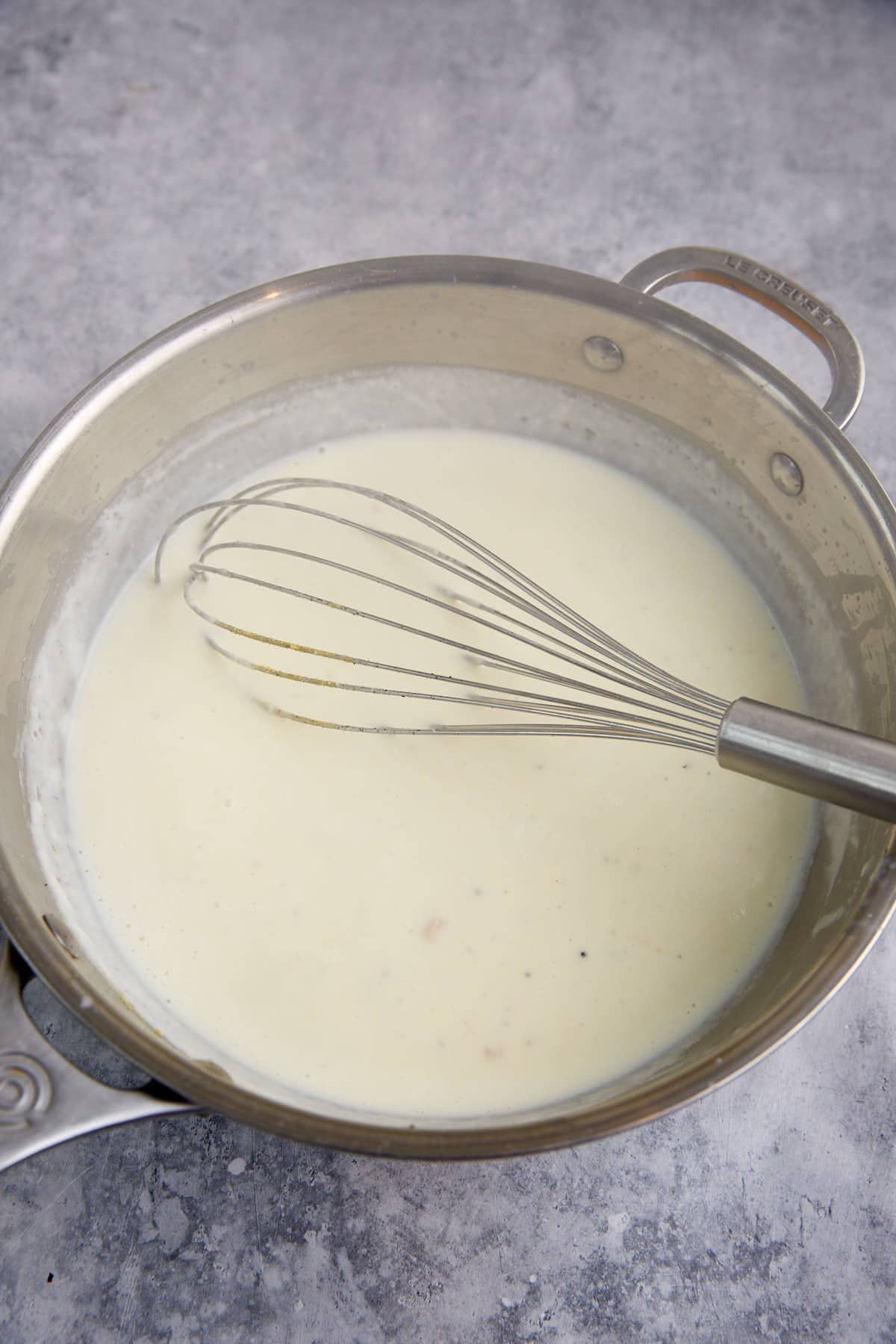 A bechamel sauce in a saucepan with a whisk.