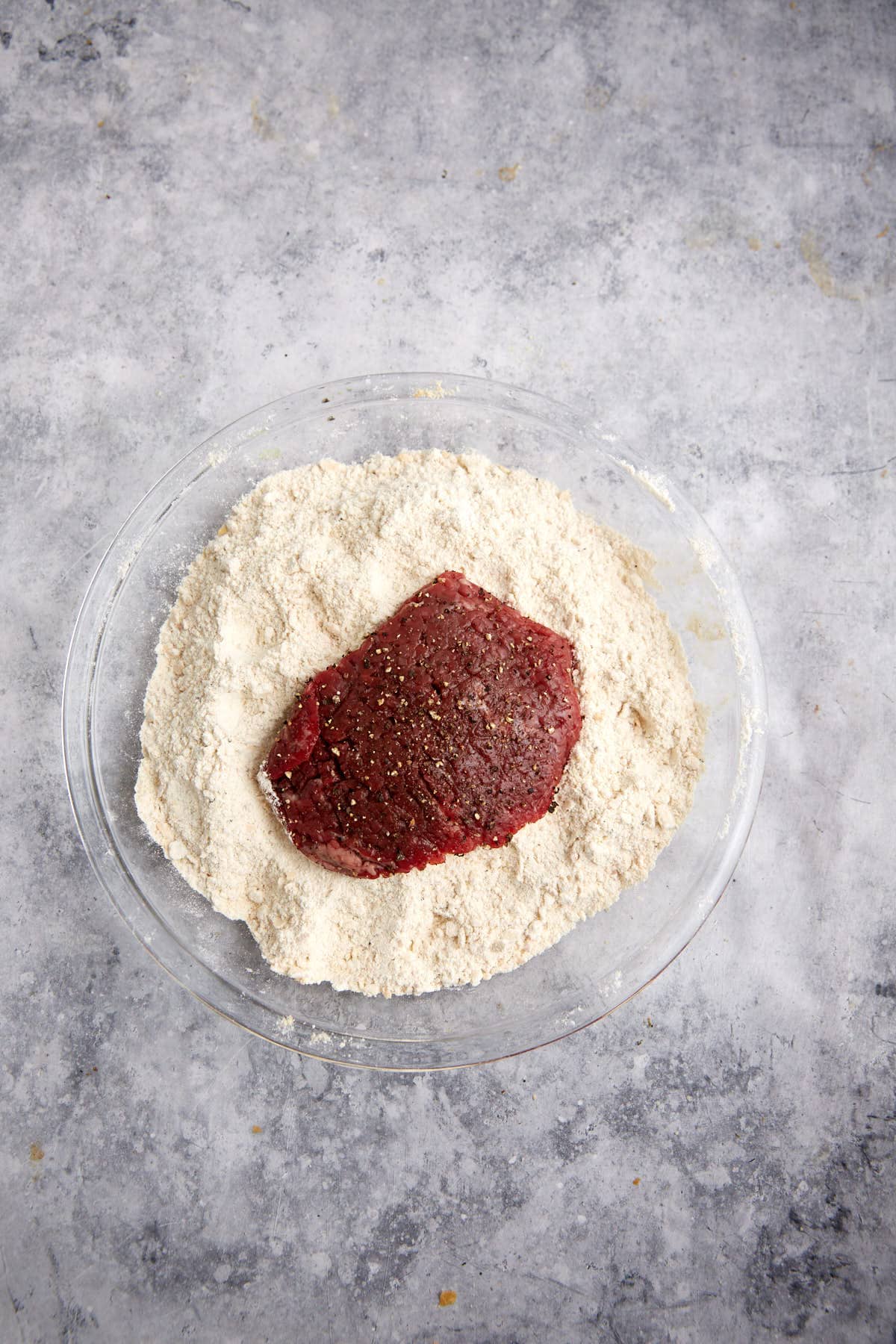 A steak in a bowl of cracker crumbs.