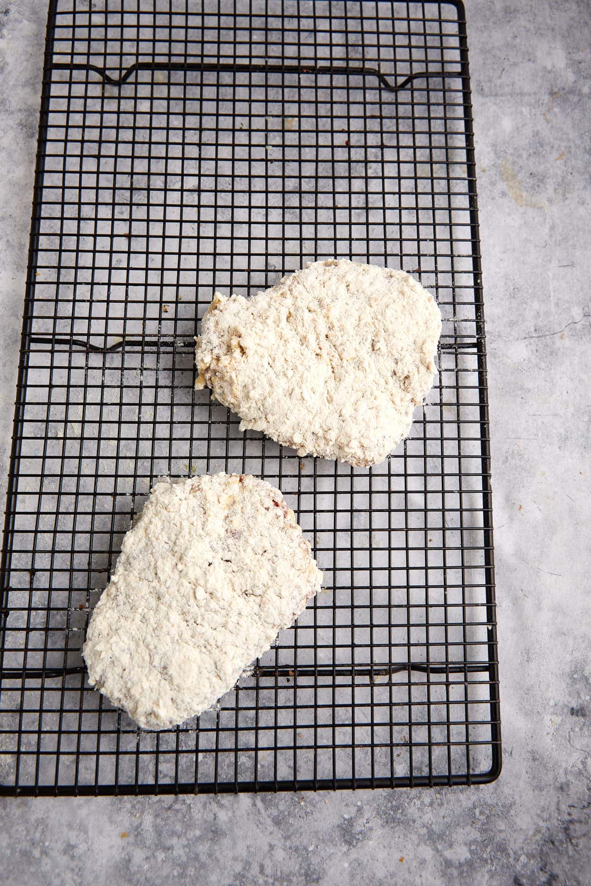 Two cubed steaks coated with cracker and flour on a rack.