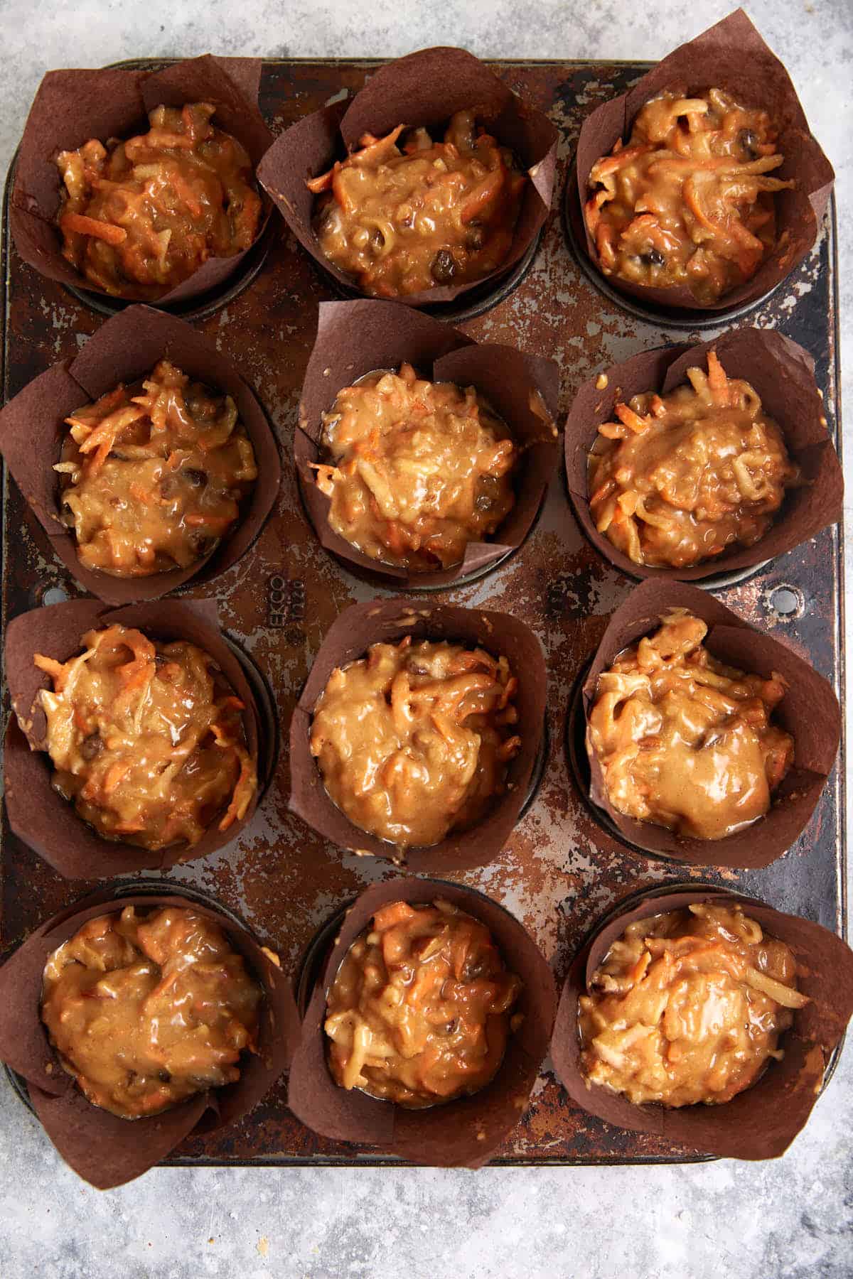 Muffin tins filled with carrot apple muffin batter.