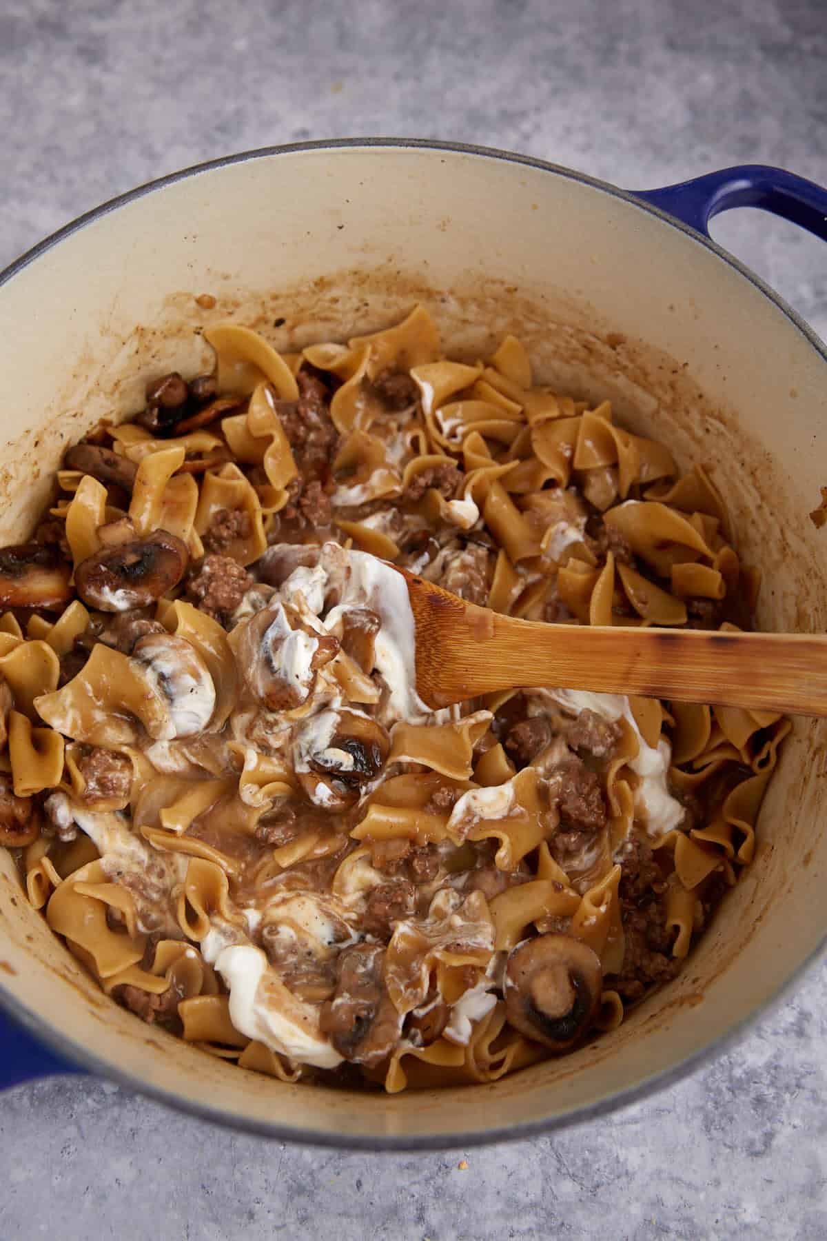 Sour cream being stirred into a pot of beef stroganoff.